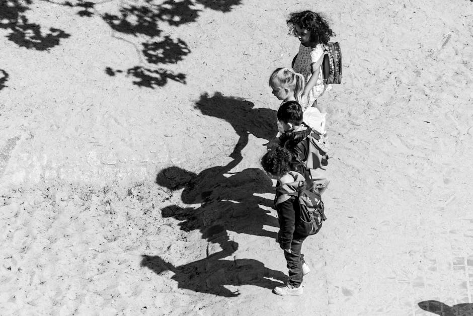 Black and white image of children in a line casting shadows on a sandy ground.