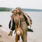 Two friends enjoy a joyful walk along the beach, embracing and smiling.